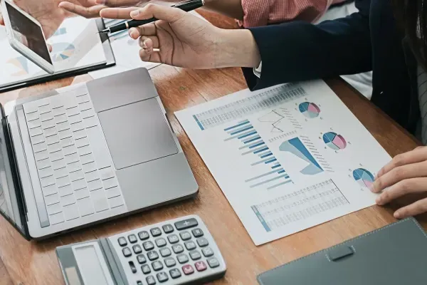 Kuvituskuva jossa työntekijällä on paperilla graafeja, edessään läppäri ja taskulaskin.